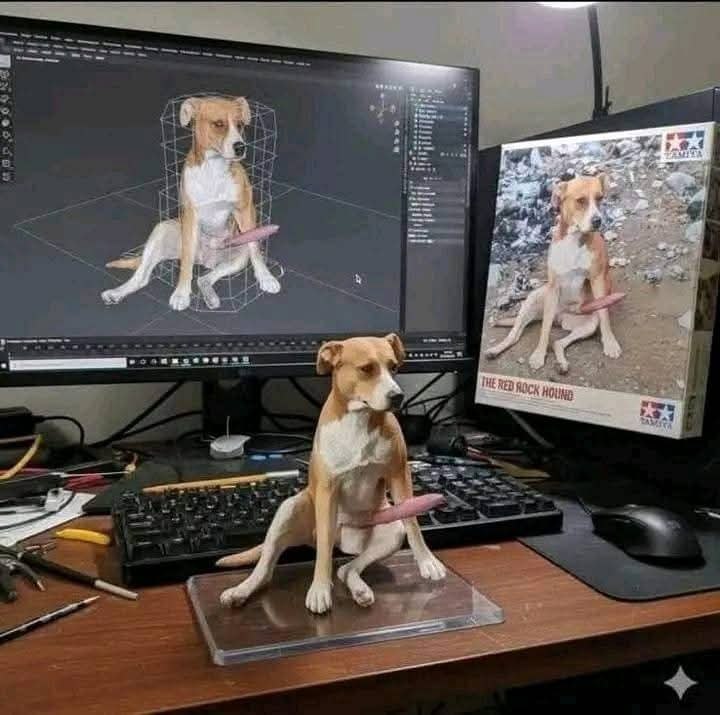 a dog sitting on top of a desk next to a computer